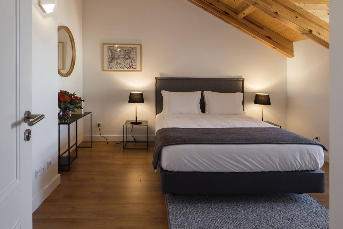 Un dormitorio con una cama, dos mesitas de noche, un tocador, un espejo y un cuadro en la pared.