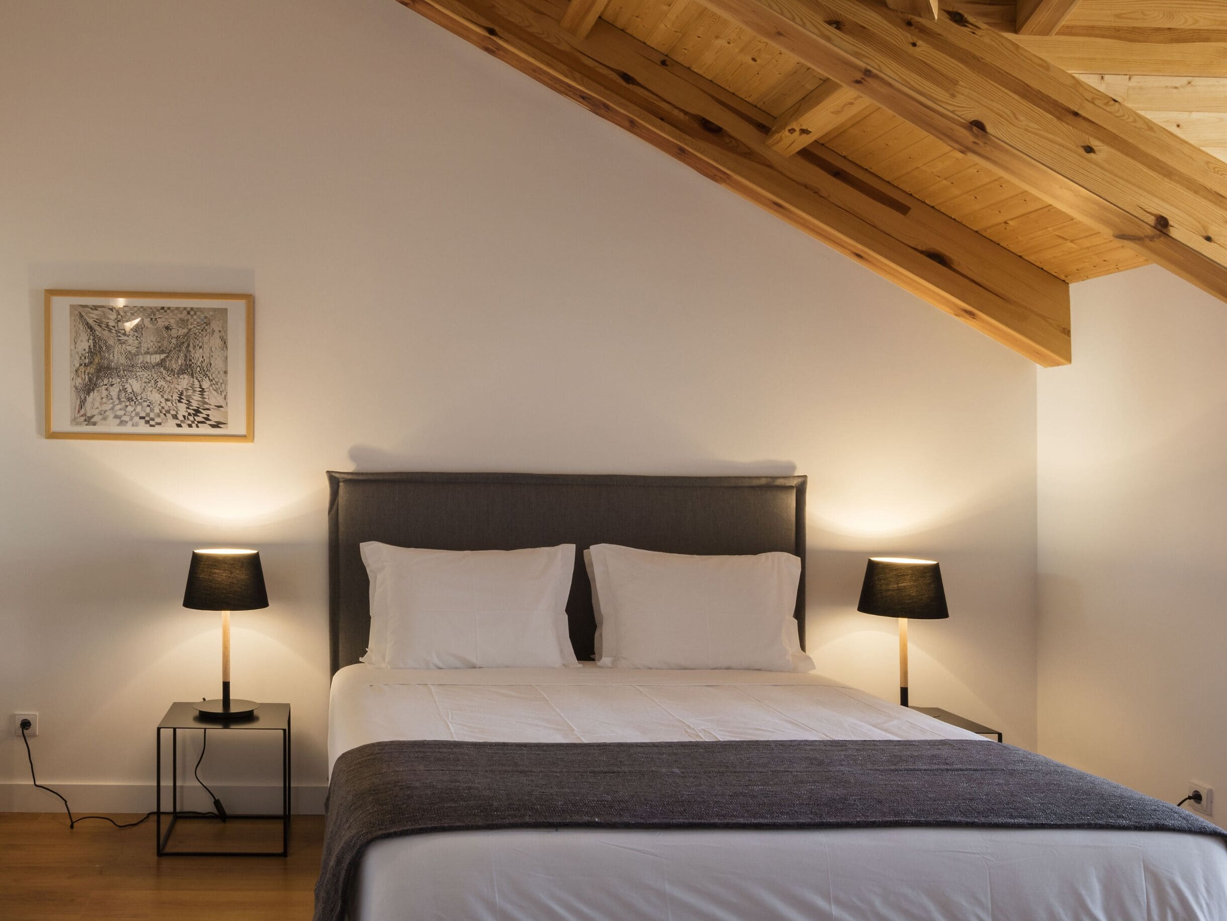 Un dormitorio con una cama, dos lámparas de noche, una obra de arte enmarcada en la pared y techo de madera.
