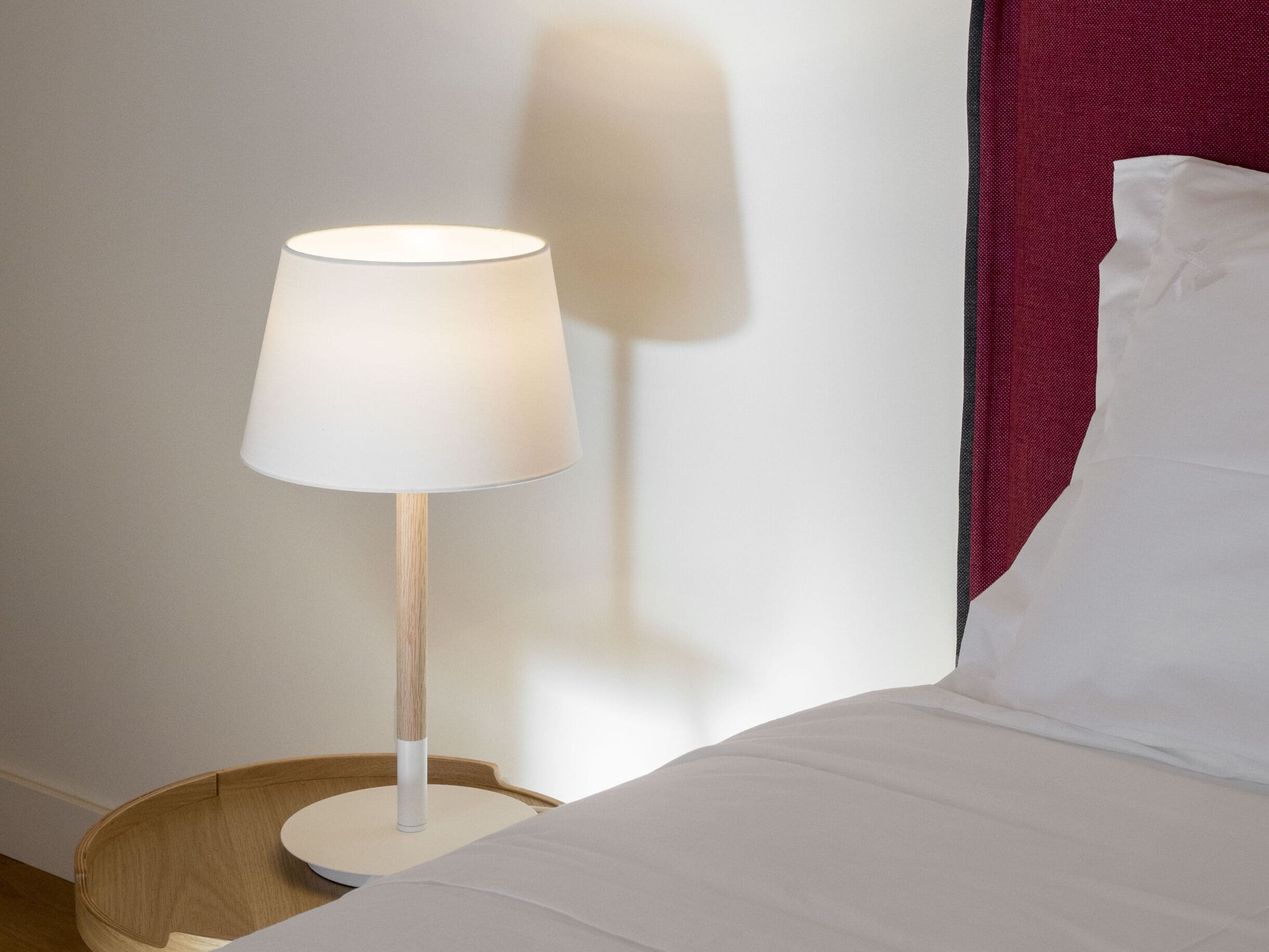 Un comodino con una lampada, un letto con biancheria da letto bianca e una testiera rossa.