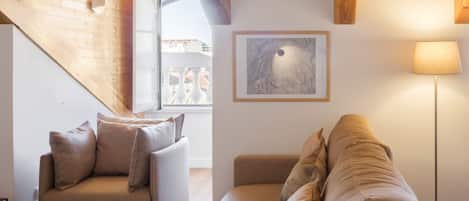 A cozy living room with a sofa and a couch, wooden ceiling beams, a framed artwork, and a floor lamp.
