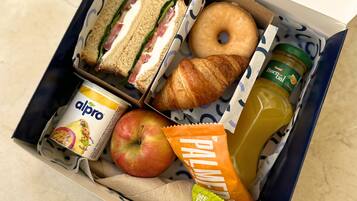 A lunch box containing sandwiches, a croissant, an apple, a juice bottle, a yogurt container, and a snack packet.