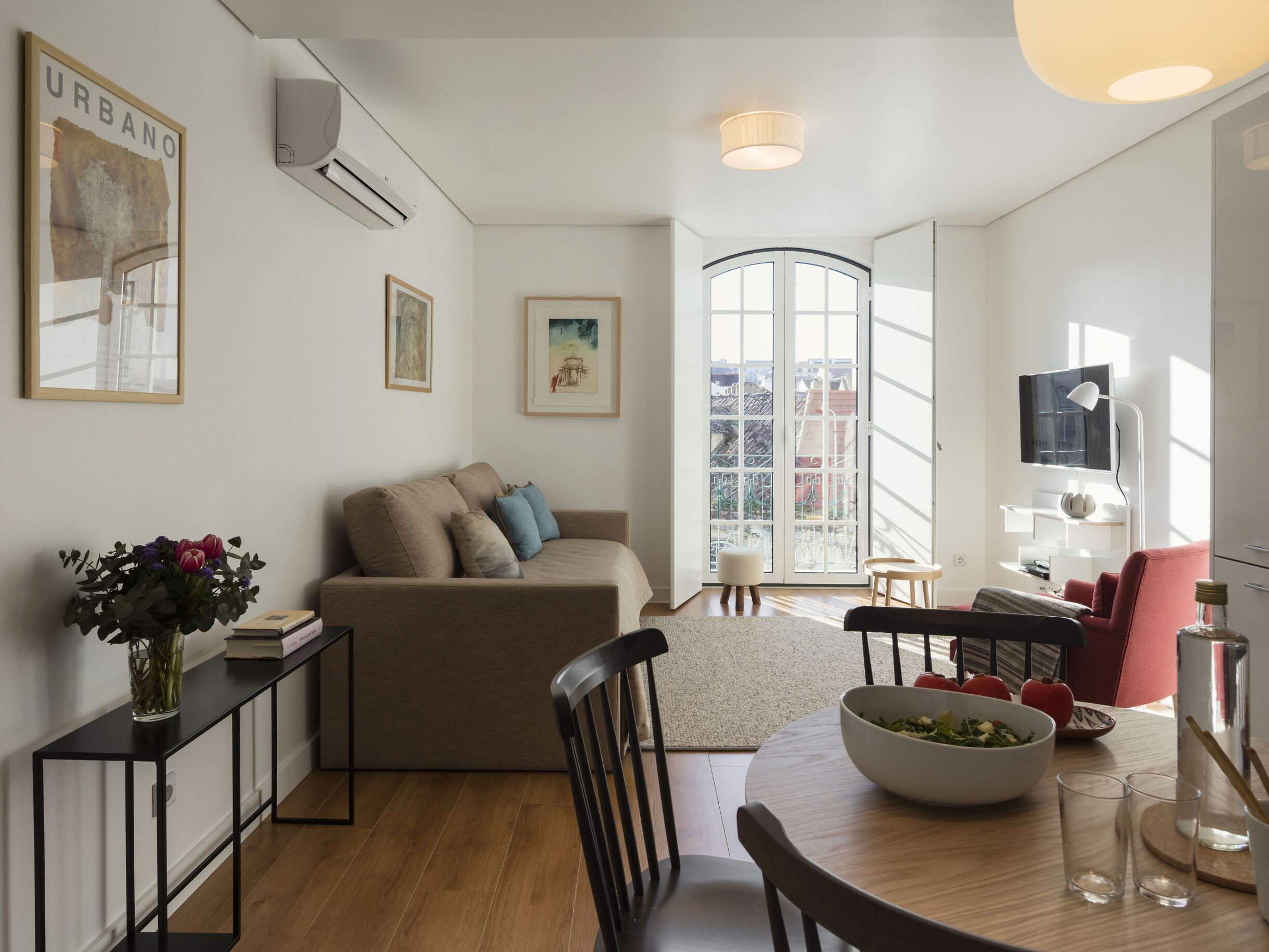 Ein modernes Wohnzimmer mit einer Couch, einem Esstisch mit Stühlen, einem Fernseher und Kunstwerken an den Wänden.