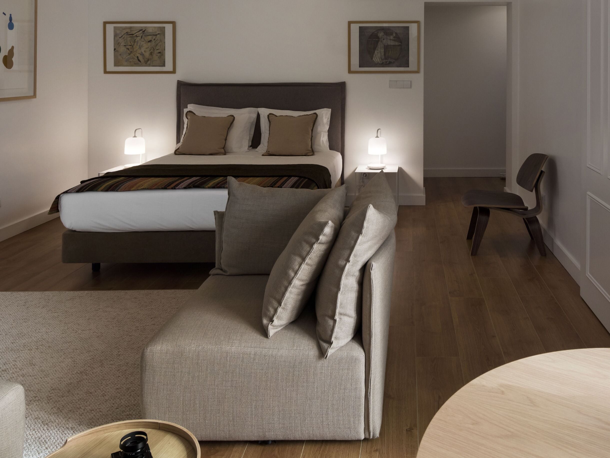 Un dormitorio moderno con cama, sofá, sillón y dos lámparas de noche.
