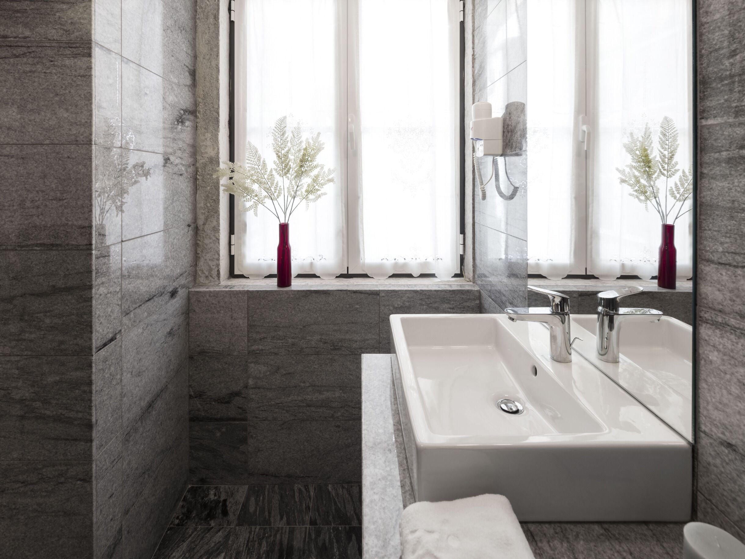 A modern bathroom with a large sink, a mirror, and a window with curtains.