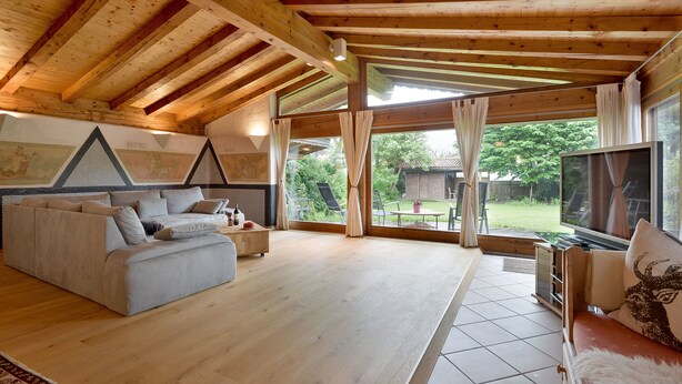 A spacious living room with a wooden ceiling, a sofa, a TV, and a view of the outdoors. - Landhaus Florian (Sankt Johann in Tirol)