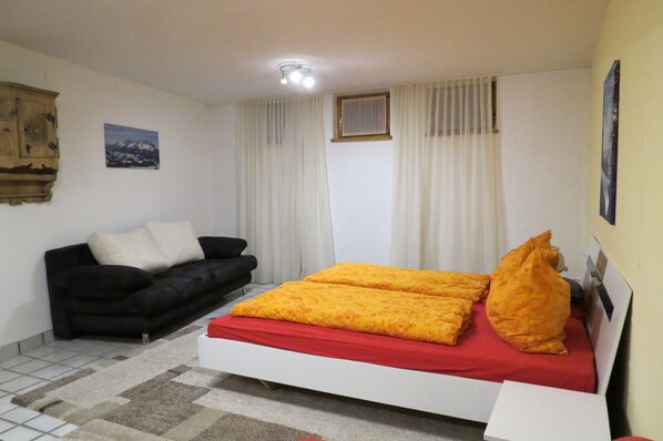 A bedroom with a bed, a black sofa, a small window, and a wall-mounted cabinet.
