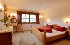 A bedroom with a wooden bed, a desk, a chair, a mirror, and a window with curtains.