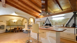 A modern kitchen with wooden beams, a central island, bar stools, and a dining area with a table and chairs. - Landhaus Florian (Sankt Johann in Tirol)