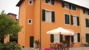 A two-story building with a bright orange facade, green shutters, and a patio area with a table and chairs. - Bed & Breakfast Lucca Fora (Capannori)