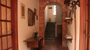 A narrow hallway with a brick archway leading to a staircase. There is a wooden desk with drawers and a sewing machine on the left, and a shelf with books on the right. - Bed & Breakfast Lucca Fora (Capannori)
