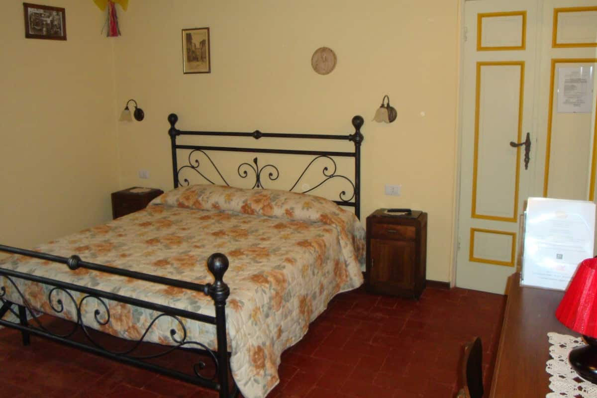 A bedroom with a bed, bedside tables, a wooden dresser, a door, and a wall with a clock and pictures.
