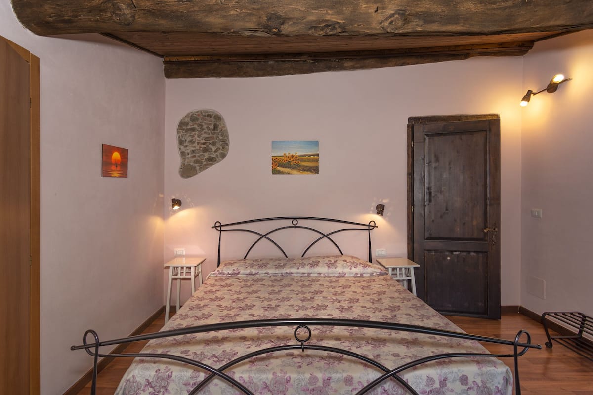 A bedroom with a bed, a wooden door, a stone wall, and two wall-mounted lights.