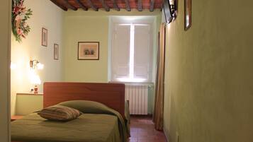 A bedroom with a wooden bed, a nightstand with a lamp, a window with curtains, and a radiator.