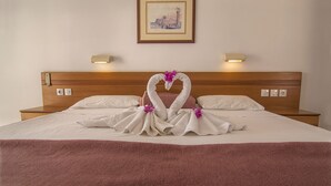 A neatly made bed with a pink blanket, two white towels shaped into swans with purple flowers, and a framed picture on the wall. - Stella View Studios (Rhodes)
