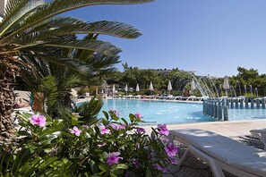 A pool area with lounge chairs and umbrellas, surrounded by palm trees and flowering plants. - Stella View Studios (Rhodes)