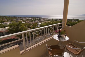 A balcony with wicker chairs, a table with a bottle and glasses, and a view of a coastal town. - Stella View Studios (Rhodes)