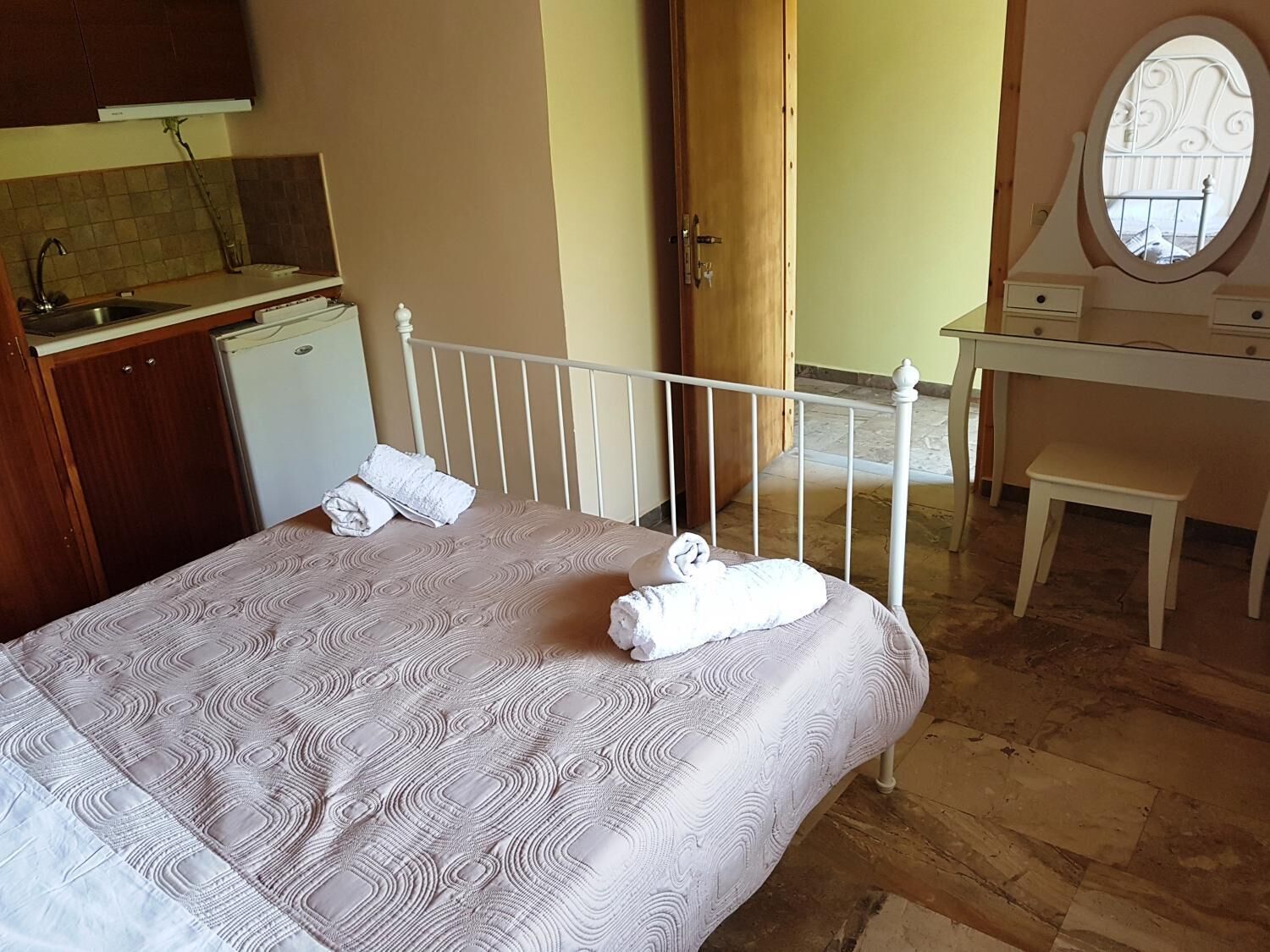 Un dormitorio con una cama, un escritorio pequeño, un espejo y una kitchenette.