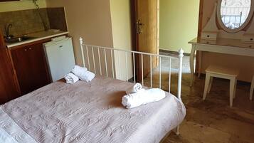 Un dormitorio con una cama, un escritorio pequeño, un espejo y una kitchenette.