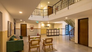 A spacious living area with a green sofa, wooden chairs, a dining table, and a kitchen area with a sign that reads 'olive'. - Treebo Trend Orchard Suites (Bengaluru)