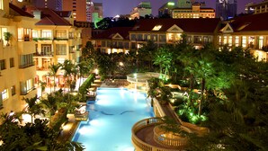 A large indoor swimming pool surrounded by lush greenery and multiple hotel buildings with balconies. - Treetops Executive Residences (Singapore)