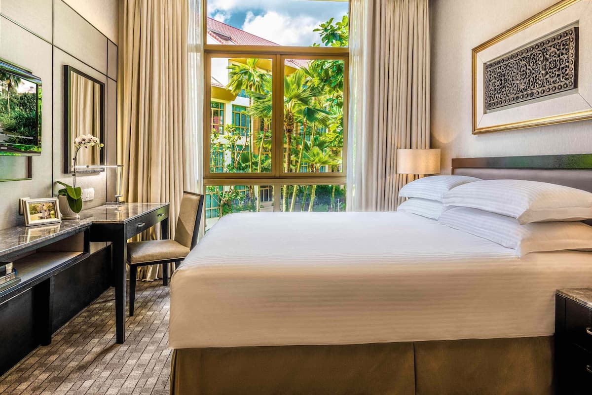A hotel room with a large bed, a desk, and a window with a view of palm trees and a building.