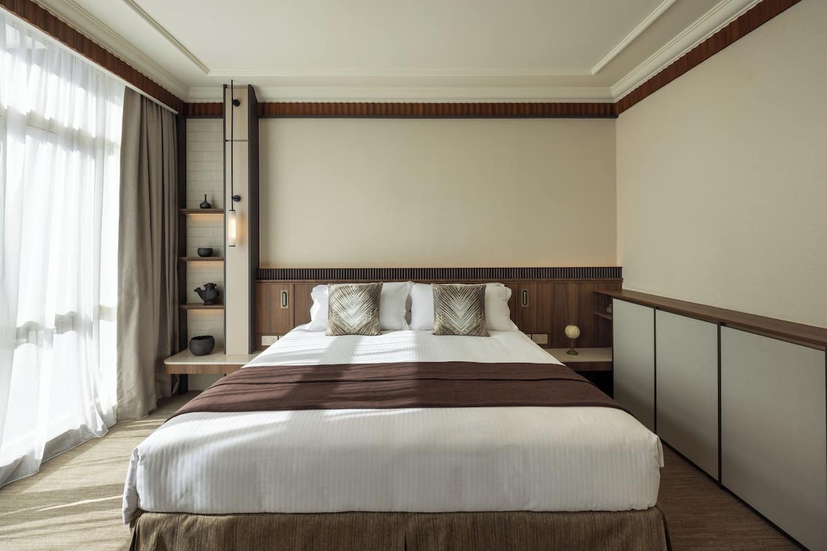 A hotel room with a large bed, a bedside table, a nightstand, a wardrobe, and a window with curtains.