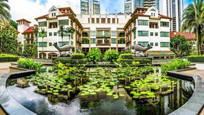 A modern hotel with a central courtyard featuring a reflective water pond with lily pads, surrounded by lush greenery and palm trees. - Treetops Executive Residences (Singapore)
