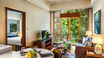A modern hotel room with a dining area, a sofa, and a large window with a view of greenery.