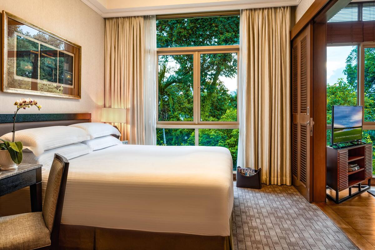 A hotel room with a large bed, a TV, a desk with a lamp, and a window with curtains.