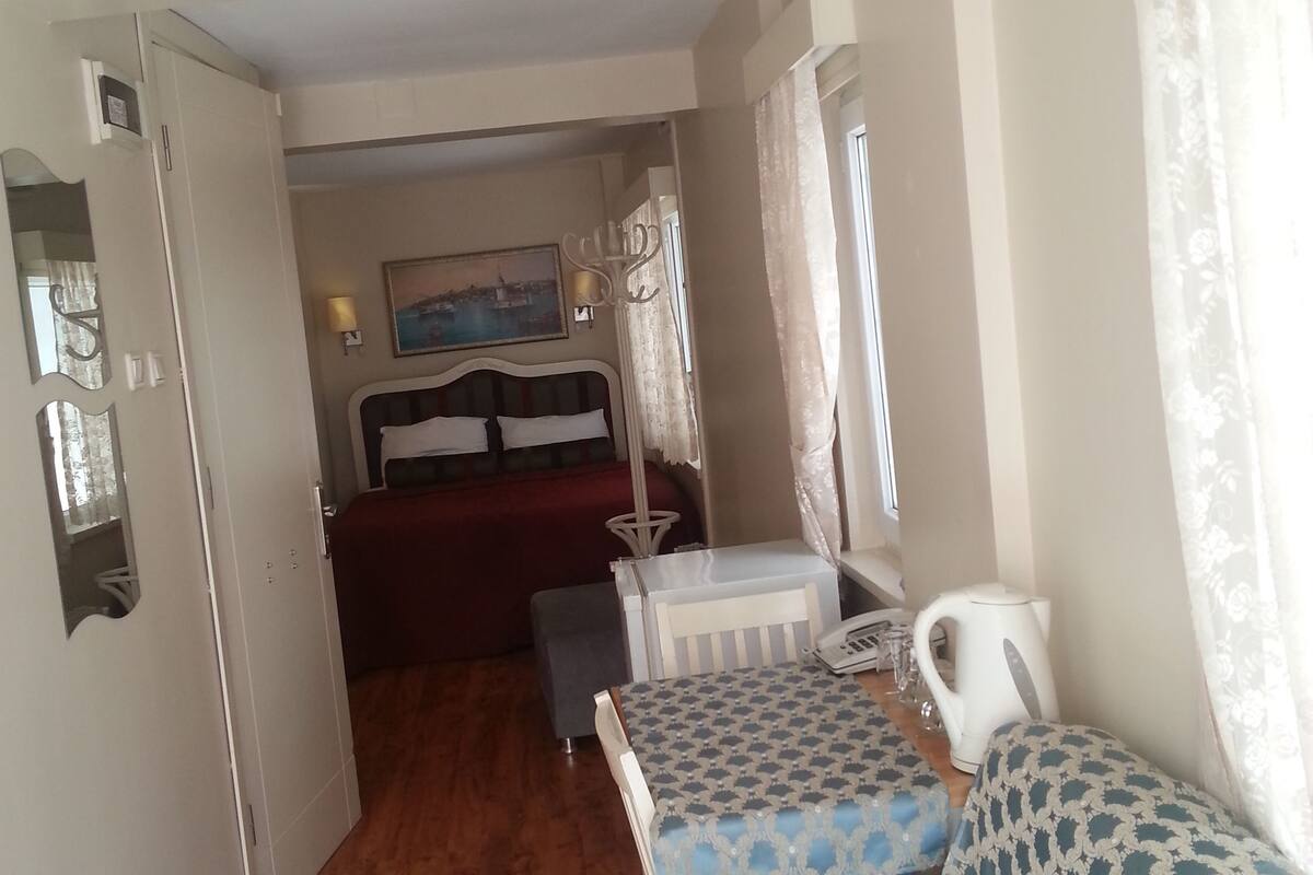 Una habitación pequeña con cama, una mesita, un sofá y una ventana con cortinas.