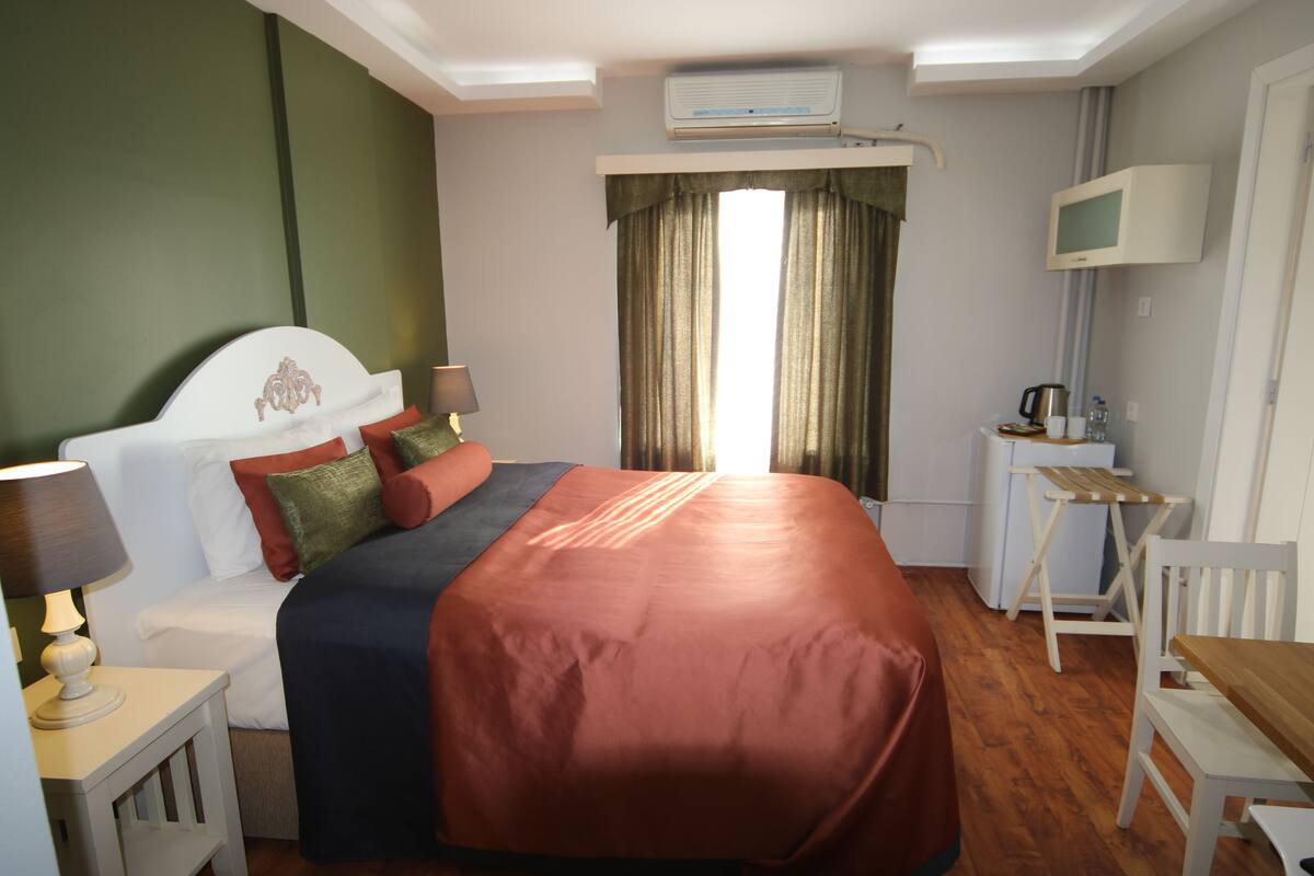 Habitación de hotel con una cama grande, un escritorio, una silla, televisión y ventana con cortinas.
