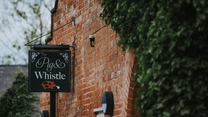 Um edifício de tijolos com uma placa que diz 'The Pig & Whistle'.