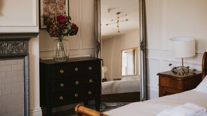 Quarto de hotel com um espelho grande, cómoda com gavetas, mesa de cabeceira com candeeiro e cama com roupa de cama branca.