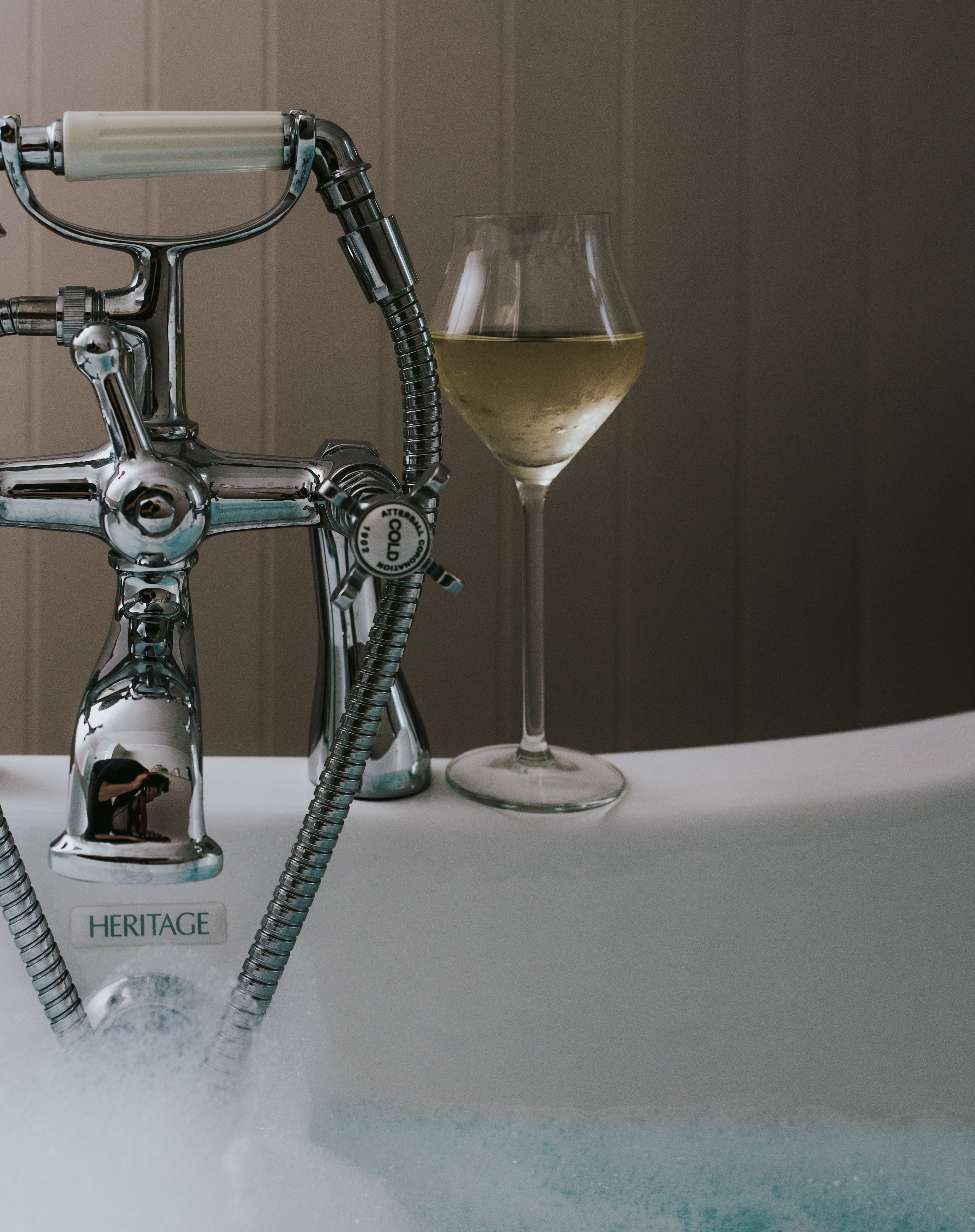A bathroom with a vintage-style faucet, a glass of white wine, and a bathtub.