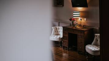 A room with a wooden desk, two white tufted chairs, a wall-mounted TV, and a striped lamp.