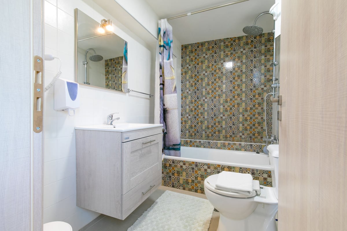 Ein Badezimmer mit Toilette, Waschbecken mit Spiegel, Duschvorhang und Badewanne.