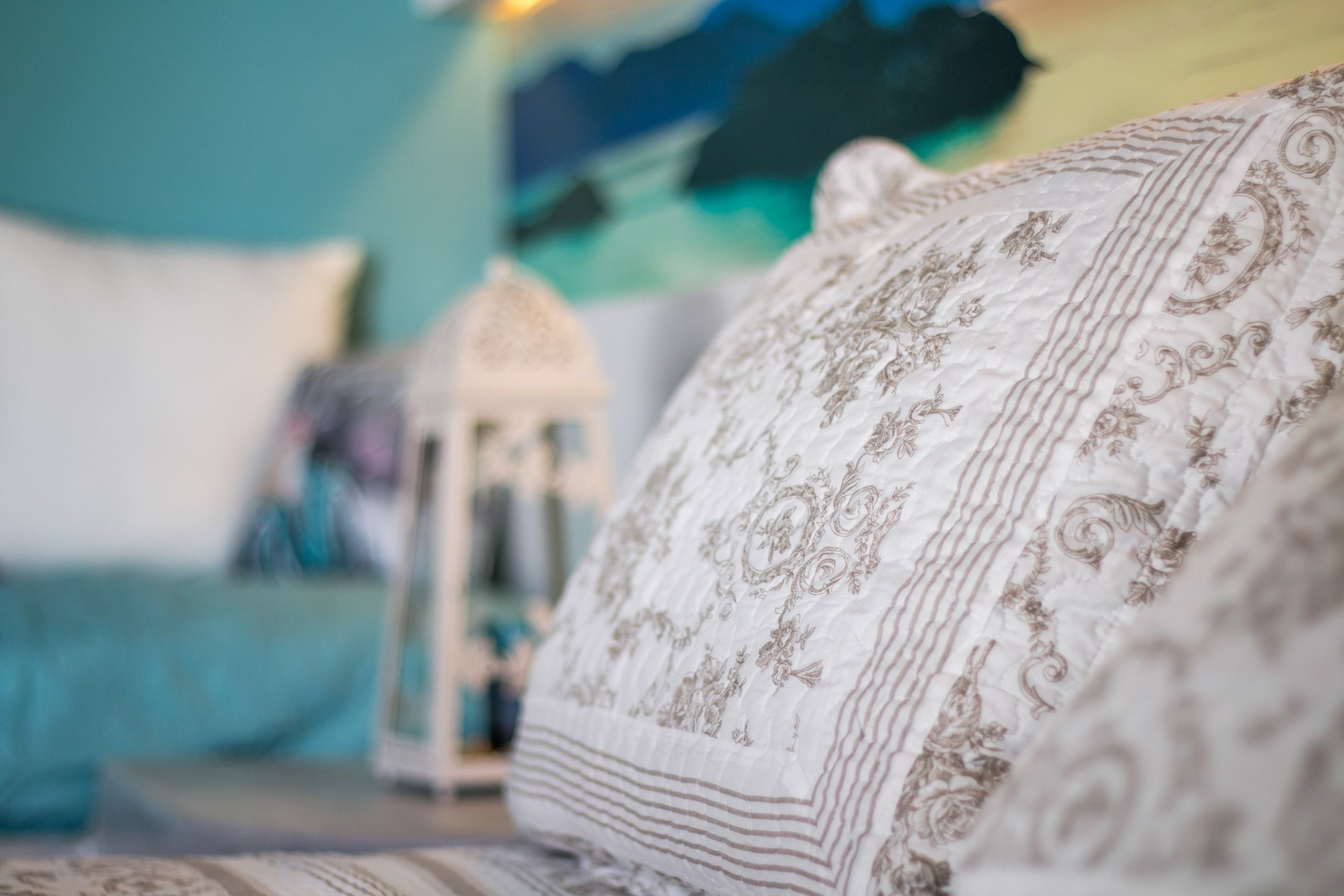 A bed with a patterned pillow and a white lantern in the background.