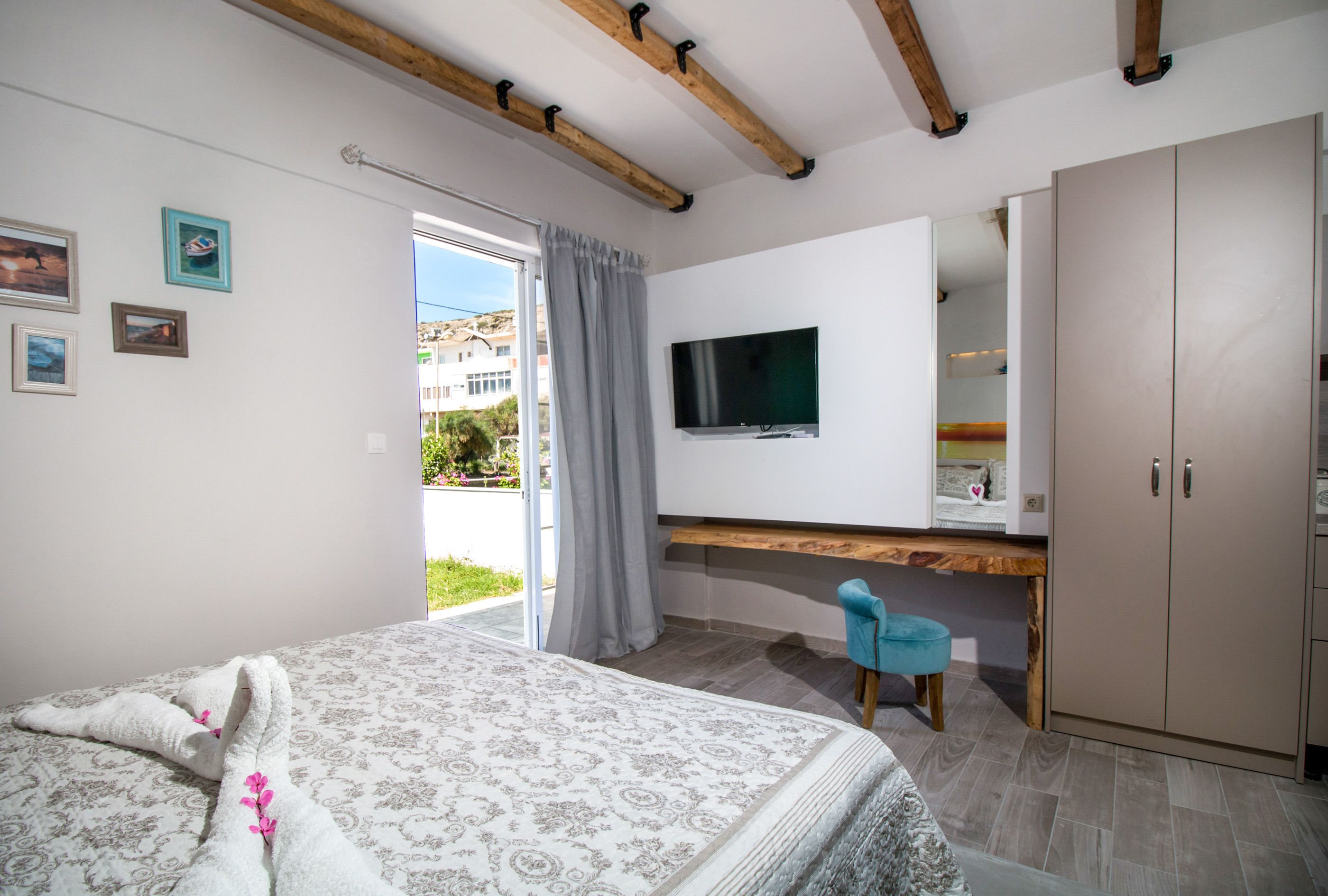 A bedroom with a bed, a TV mounted on the wall, a wardrobe, and a window with curtains.