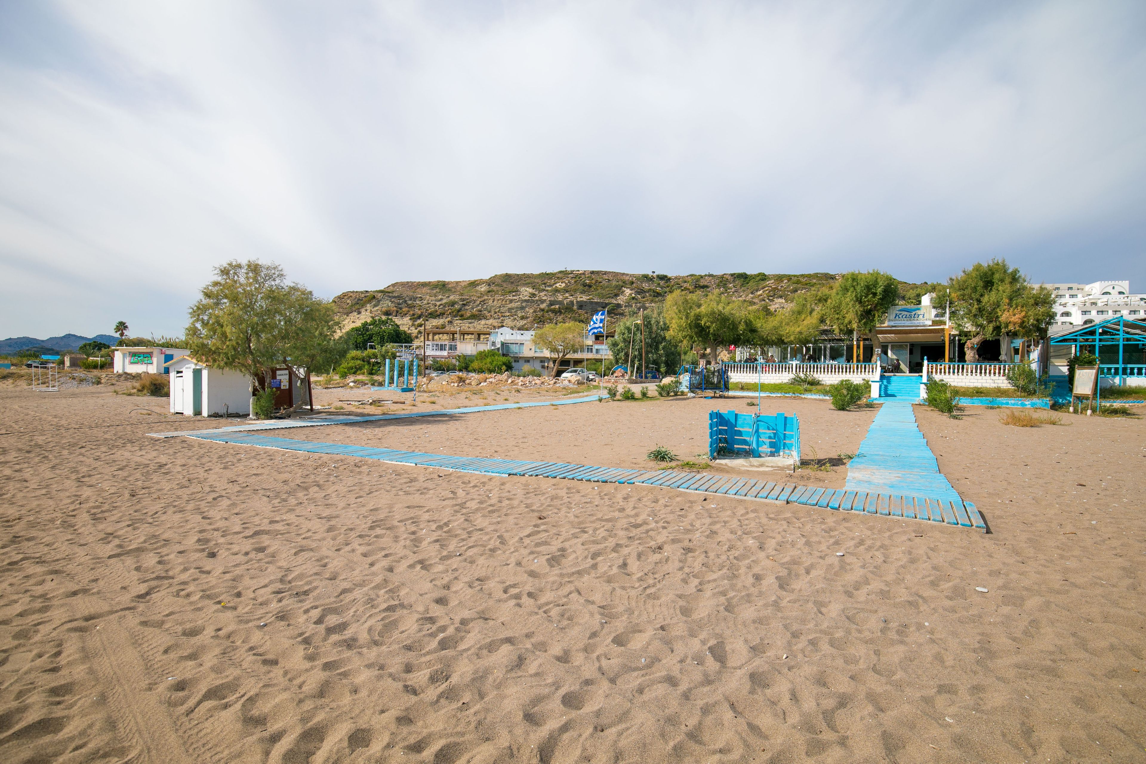 A sandy beach with a blue pathway leading to a building with a sign that reads "Kosta".