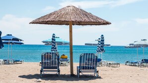Ein Strand mit gestreiften Liegestühlen und Sonnenschirmen, ein reetgedeckter Sonnenschirm und Blick auf das Meer.