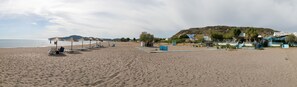 A beach with sun loungers and umbrellas, a small kiosk, and a building with a sign. - Kastri Boutique Beach (Rhodes)