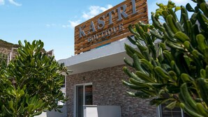 Ein hölzernes Schild mit der Aufschrift "KASTRI Boutique" über einem Gebäude mit einer Steinfassade und einer Tür.
