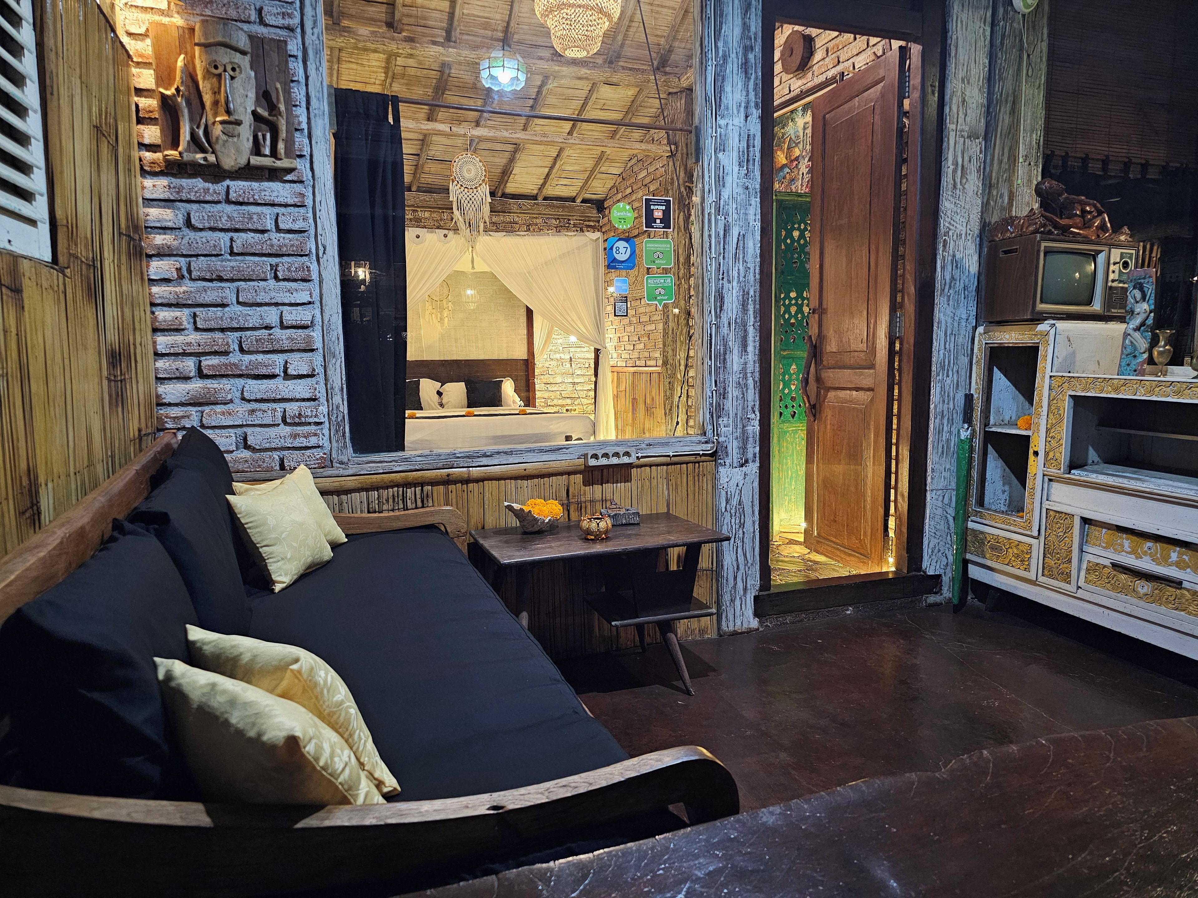A room with a bed, a table with flowers, a television, and a rustic brick wall.