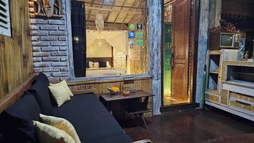 A room with a bed, a table with flowers, a television, and a rustic brick wall.