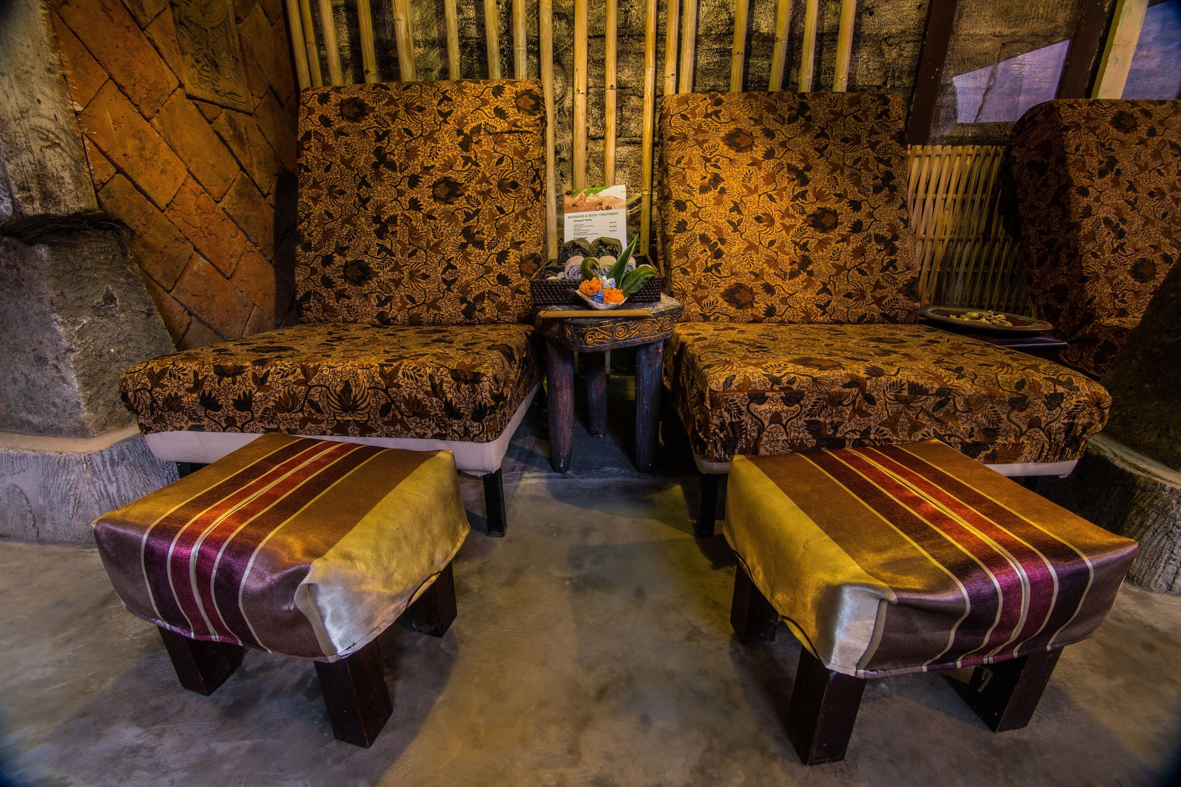 A room with two sofas and two matching ottomans, a small table with a sign, and a bamboo wall.