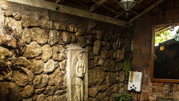 A stone-walled bathroom with a bathtub filled with flower petals, a stone statue, and a wooden ceiling. - Santhiku Hotel & SPA (Banjar)