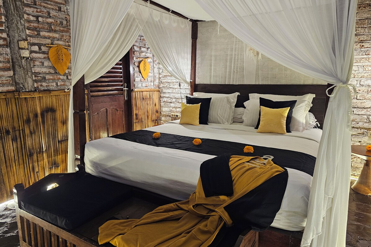 A bed with a canopy, a wooden bench, and a brick wall.