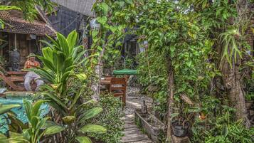 A lush garden with a wooden staircase leading to a pool area, surrounded by dense foliage and tropical plants.