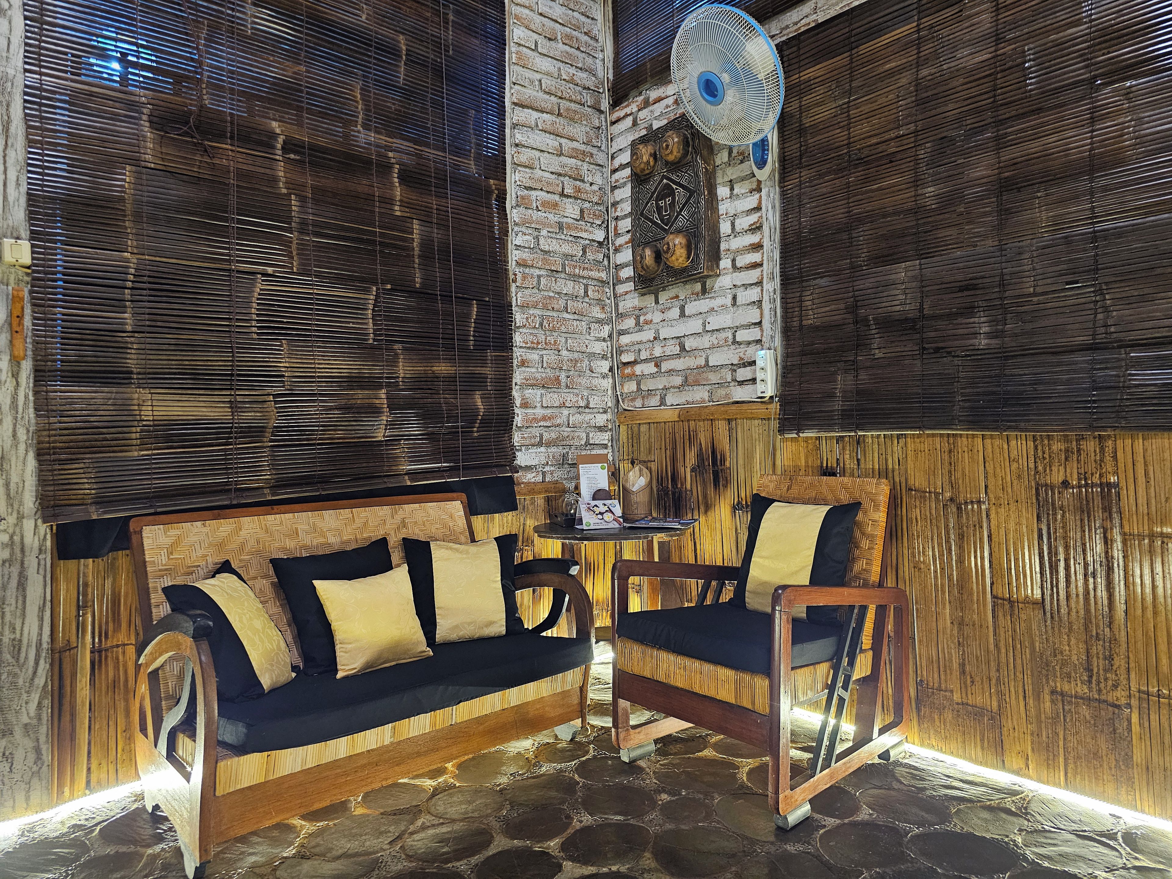 Una habitación con sofá, sillas, un ventilador y una pared de ladrillo.