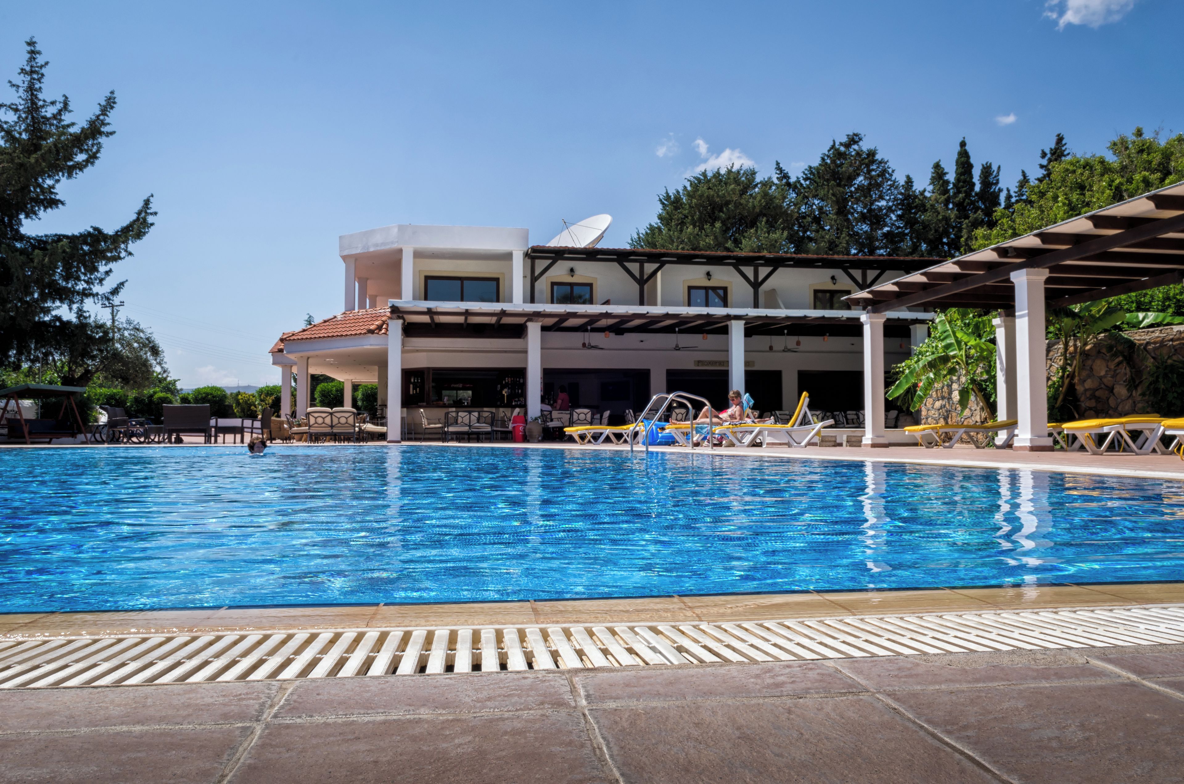 A swimming pool with a covered area, lounge chairs, and a building with a satellite dish in the background.